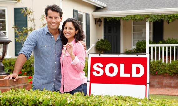 A couple standing in front of their home with the sold sign.